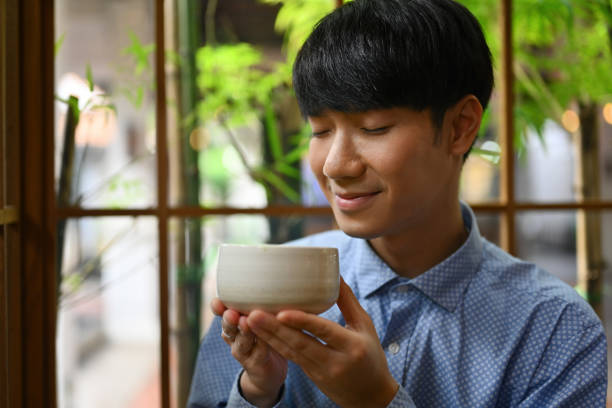 gros plan avec un jeune homme asiatique appréciant et tenant une tasse de thé, du thé matcha traditionnel japonais. - green tea tea zen like japan photos et images de collection