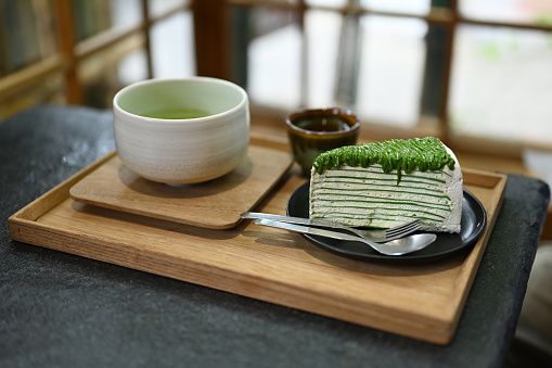 Close up image of slice of Matcha crepe cake with Genmaicha Uji latte in the Japanese tradition ceramic bowl.