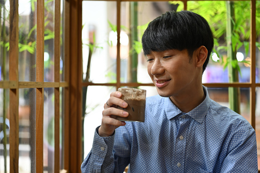 Portrait with gentle looking of Young Asian man enjoying hojicha latte in the modern Japanese cafe.