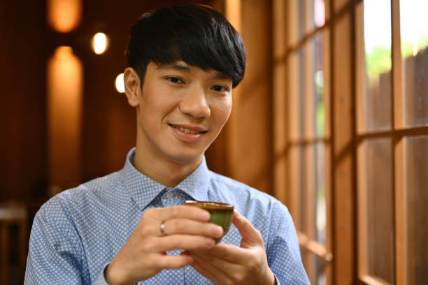 portrait avec un jeune homme asiatique dégustant un thé chaud dans des tasses à thé traditionnelles en argile. - green tea tea zen like japan photos et images de collection