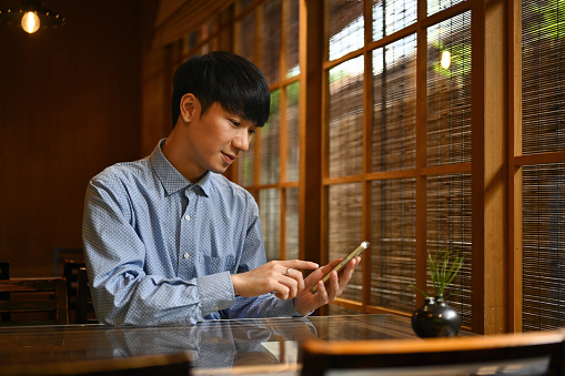 Portrait with Smart looking of Young Asian Businessman using smartphone in a cafe decorated in Japanese style.