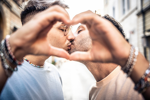 Young gay couple kissing making heart symbol with hands - Happy homosexual guys celebrating pride day together - Lgbt concept