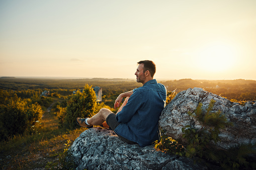 Adult man enjoying sunset sitting on top of the mountain