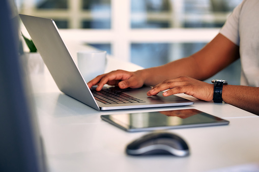 Cropped image of a man, freelancer, businessman, or call center worker working while sitting at a laptop at a desk in an office or coworking space. Remote work from home.