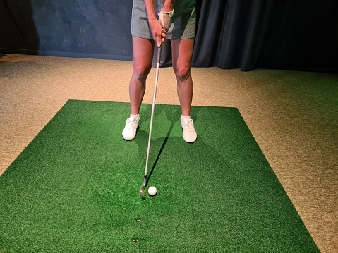 Professional female golfer playing golf indoors on golf simulator closeup. Driving range with screen and golf course