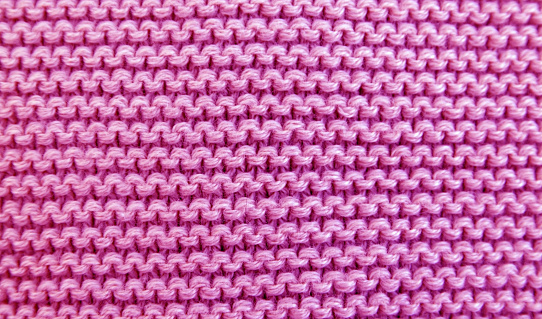 Close up background of knitted pink wool fabric knitwear texture. Selective focus.