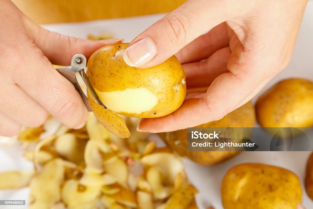 Peeling potatoes with a small silver peeler Woman hand peeling pomato with a peeler on the table. Peeling Food Stock Photo