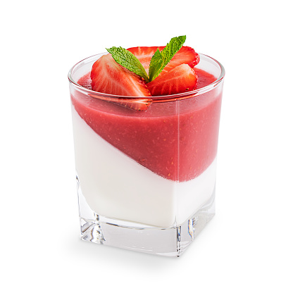 Italian homemade healthy panna cotta dessert of cream thickened with gelatin with layer of strawberry sauce served in glass garnished with sliced berries and mint leaf isolated on white background