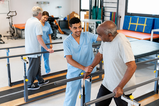 Senior patients walking with the help of parallel bars and their physical therapists - Healthcare concepts