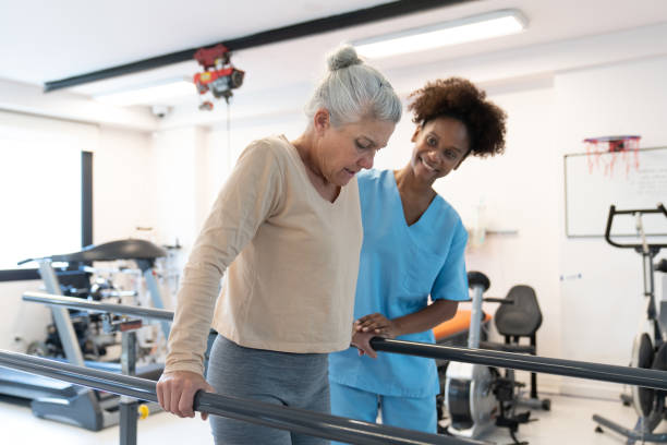 istock Cheerful therapist encouraging senior female patient walk while leaning on parallel bars during physical therapy 1594515139