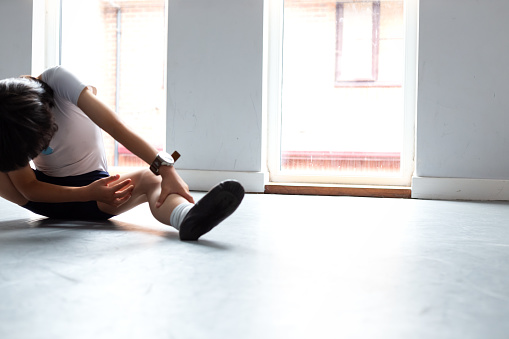 a little boy aged 6 is doing his ballet basic movement, Stretch and bend his legs. Classic Ballet. He is wearing Navy Dance shorts, White cap sleeve leotard, white ballet socks and black ballet shoes.