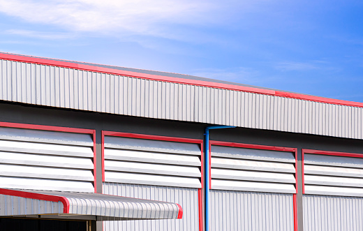 Aluminum Louvers and rain drain pipe on corrugated steel wall with roof eaves of industrial warehouse Building against blue sky background