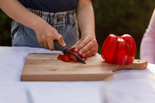 Close up shot of unrecognizable little girl using a knife and cutting up a red bell pepper.