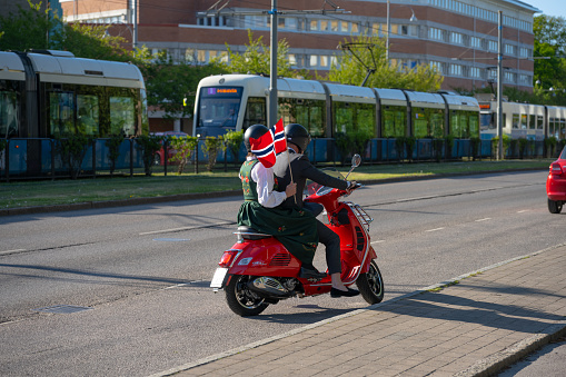 Gothenburg, Sweden - May 17 2023: Couple on a red scooter holding a Norwegian flag.