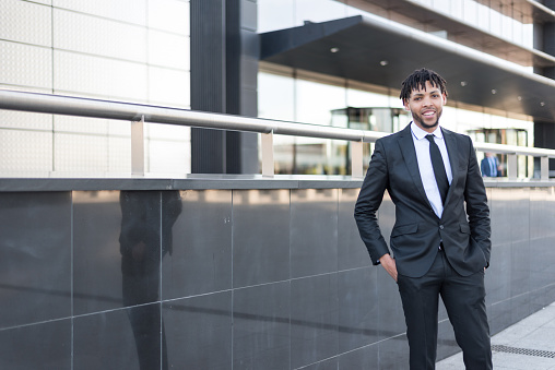 black Confident businessman wearing suit and standing at office area in city looking at camera