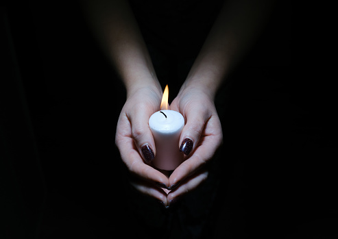 a burning candle in female hands folded in prayer