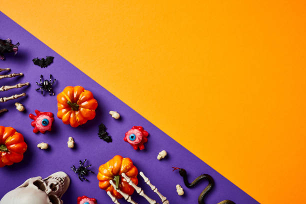 istock Happy Halloween concept. Flat lay pumpkins, skeleton hands, bloody eyes, skull on split violet and orange background. 1594629123