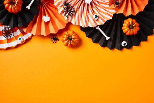 istock Halloween flat lay composition with paper fans, pumpkins, ghosts, bones on orange background. 1594651093