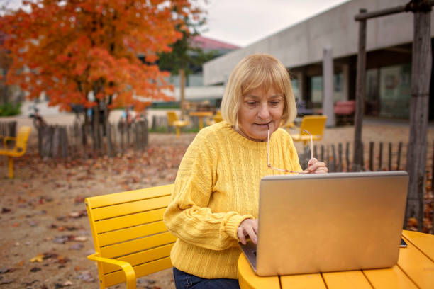 年配の女性は秋の公園でノートパソコンを使う。デジタル時代、技術に精通したシニアおよび最新のテクノロジー - senior women electronics people remote control ストックフォトと画像