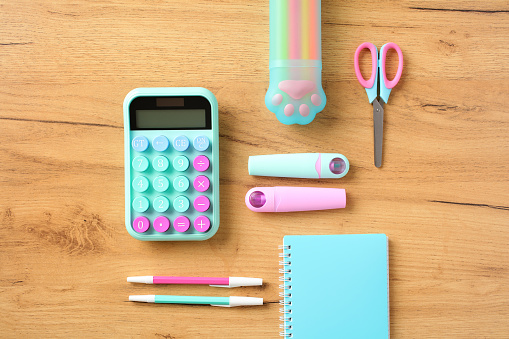 Creative layout with pink and turquoise school supplies, notebook, calculator on wooden background. Flat lay, top view. Back to school concept.