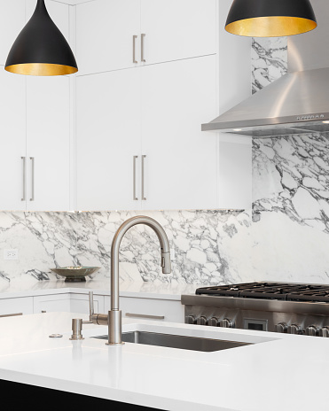 A kitchen detail with white cabinets, modern light fixtures hanging over a black island, and a marble countertop and backsplash.
