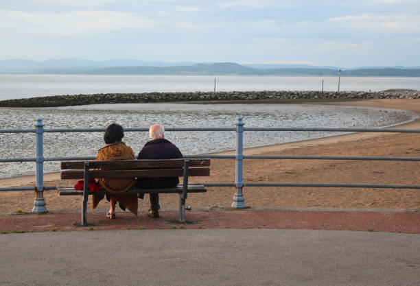 zwei ältere menschen auf einer bank, auf der stadtpromenade, blick auf die bucht von morecambe. - morecombe bay stock-fotos und bilder