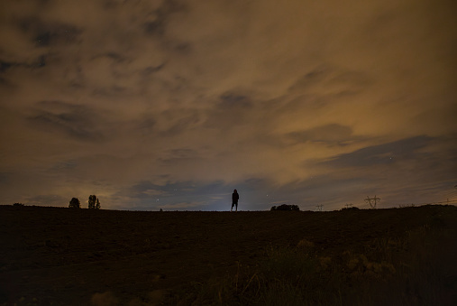 Silhouette of a man standing under the stars on a cloudy night