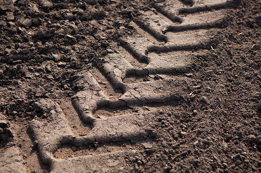 Close-up of a tractor wheel print in dark soft ground, in an agricultural field.