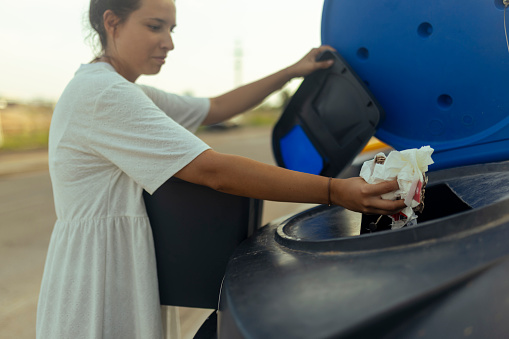 Woman throwing carton package into blue garbage recycle bin outdoors, eco-friendly woman caring about environment