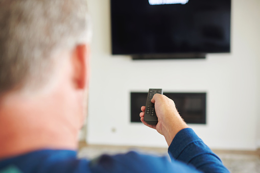 Unidentifiable male using a remote control to change the channels on a TV