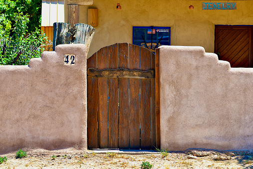 Ranchos de Taos, New Mexico, USA - July 24, 2023:  Traditional and decorative wood door and adobe wall outside a closed jewelry store.