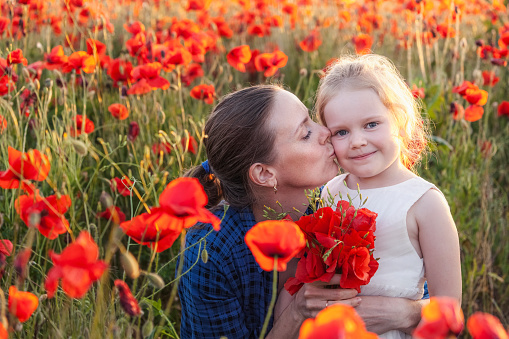 Little girl and her mother with a bouquet of poppies in a field on a summer day