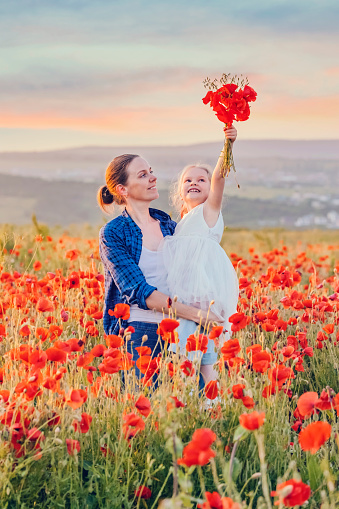 Little girl and her mother with a bouquet of poppies in a field on a summer day
