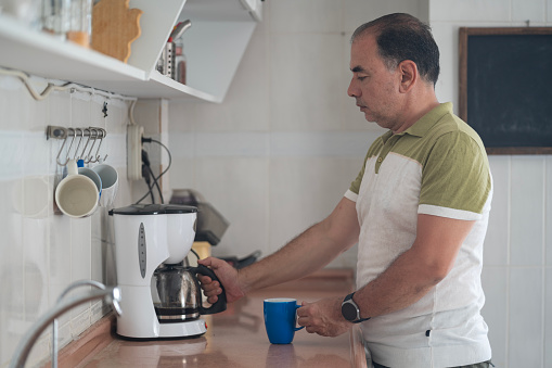 Photo of mature adult man using coffee machine for preparing coffee in domestic kitchen. Shot under daylight with a full frame mirrorless camera.