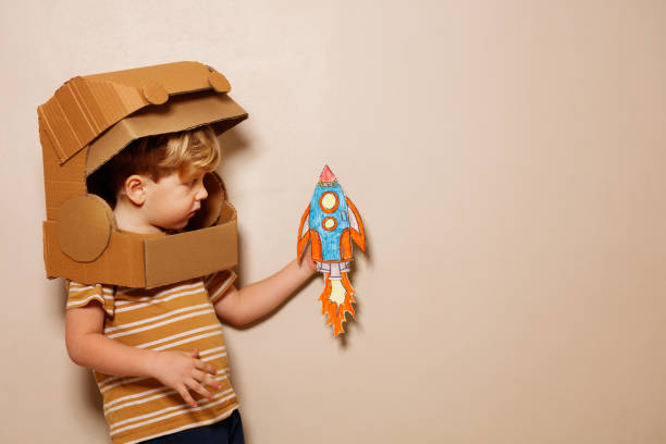 istock Cute boy plays paper rocket, wears cardboard astronaut helmet 1594924256