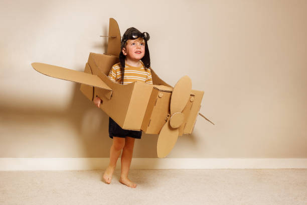 istock Young boy hold cardboard plane wears hat, glasses, pretends fly 1594924613