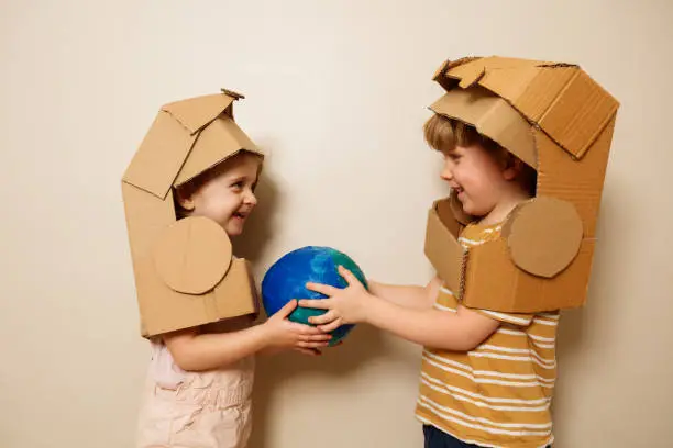 Dos niños con cascos de astronauta de cartón sosteniendo un globo terráqueo.