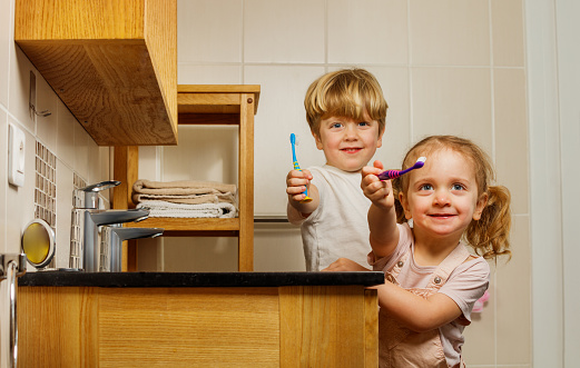 Two happy siblings, a sister, brother, are captured on camera while brushing teeth and showing off their smiles to the viewer