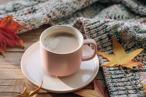 Coffee cup, autumn leaves and knitted sweater on wooden table. Fall concept. Top view.