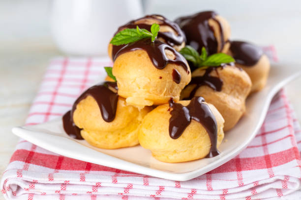 istock Delicious profiteroles with chocolate and white plate. Selective focus image on light background. 1594972041