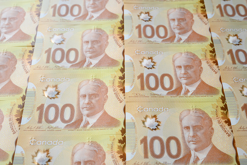 Rows of neatly lined up, overlapping Canadian one hundred dollar ($100) bills.