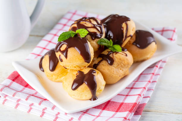 istock Delicious profiteroles with chocolate and white plate. Selective focus image on light background. 1594988219