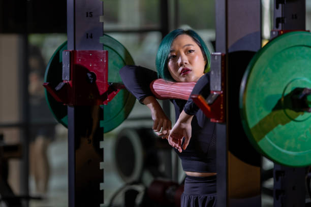 istock Asian woman is facing overtraining syndrome on practice weight lifting using barbell for arm and core muscle inside gym with dark background for exercising and workout 1594996971