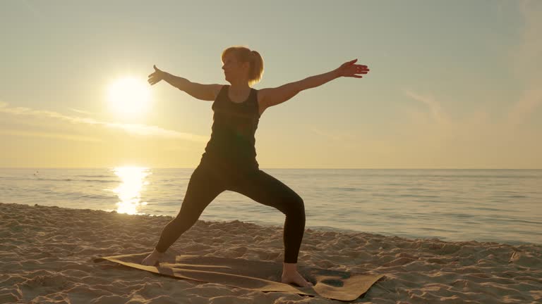 Middle years woman practice medicine yoga in meditation pose on sea beach lotus position asana balance kundalini energy