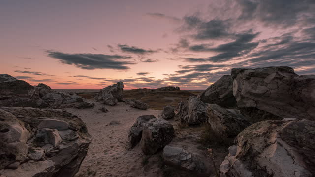 Timelapse of a beautiful sunset and the movement of clouds over boulders of rocks in an arid area.
