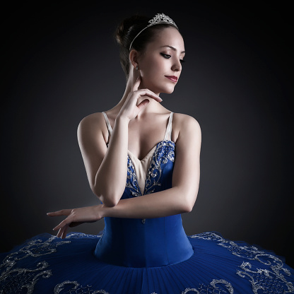 Close-up portrait of a classic ballerina in her tutu dress on dark grey background. She is standing in elegant ballet pose.