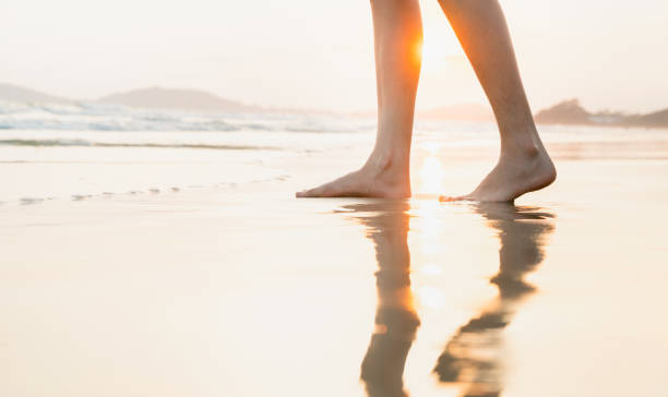 istock Woman's legs stand on the beach at sunset time. 1595413416