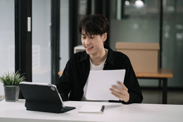 istock Employee, working with documents sitting at desk using laptop and smartphone at work. 1595507204