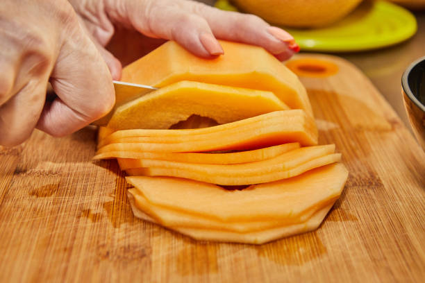 istock Chef cuts melon into slices on wooden board in the kitchen 1595552134