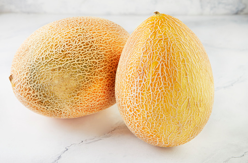 Two melons on light marble in home kitchen.